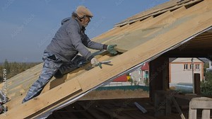 Construction work. Installation of insulation for insulation of the roof of a private house. Use of mineral wool. Laying of multi-layer thermal insulation material. Insulation of a private house with