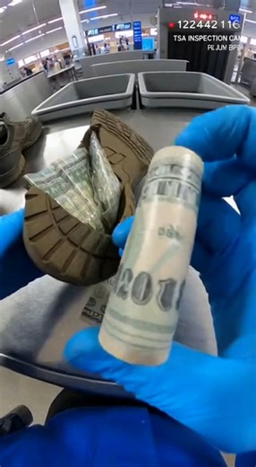 Attention is drawn to a shoe flagged during TSA inspection. The sole appears thicker than expected. The inspector applies pressure along the bottom of the shoe. The material does not compress evenly. The shoe is cut open along the sole. An interior layer becomes visible. The inspector pauses and adjusts angle to inspect further. Stitching appears deliberate. The camera captures cash sewn into the sole. Bills are folded tightly within the lining. More currency remains embedded deeper inside. The 