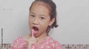 Close-up shots of adorable Asian kid who is brushing her teeth in the morning. Her front view shows an adorable face with joy and a clean smile for routine dental caring in bright bathroom.