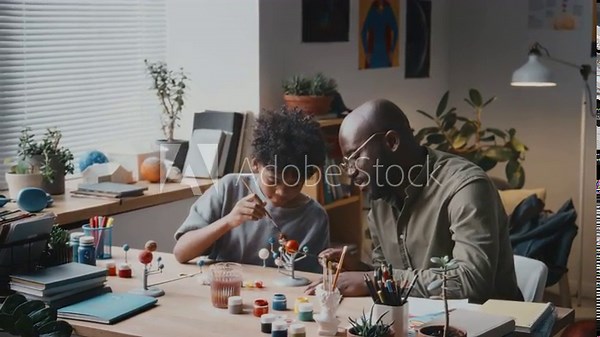 Cheerful African American man talking to little son and ruffling his hair while making DIY solar system model together at home Stock Video