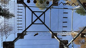 Intrepid children having fun with suspended rope bridge at wooden structure of adventure park. Low angle looking up scene