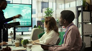 Diverse group of professionals meeting to discuss a new development strategy, utilizing infographics and monthly analysis numbers to reach target and accomplish organizational goals. Camera B.