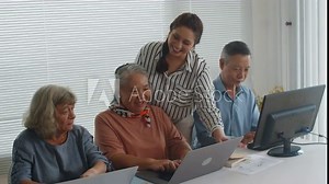 Medium long shot of young female tutor giving instructions to mature woman about laptop settings during group class