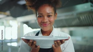 Portrait of young beautiful female chef showing her food to camera at kitchen with beautiful smiling. Chef, Lifestyle, Education, Happiness, Cheerful concept.