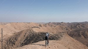 Mountain Biking Downhill steep narrow rocky ridges with scenery in the wild alone near the Dead Sea lake and Arad Mountains in the Negev Desert, Israel with bright blue sky Aerial Active Track Follow