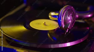 Head with an old gramophone needle on a vinyl disc close-up. Portable wind-up gramophone. A gramophone with a handle. An old gramophone with a record. In the neon light