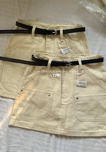 High-waisted cream denim skirt with front pockets and a black belt.