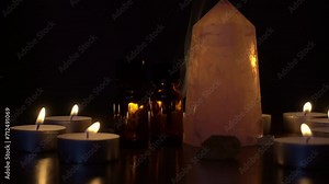The rose quartz crystal is illuminated by candles. Vials with essential oil next to rose quartz and smoke from aroma sticks.