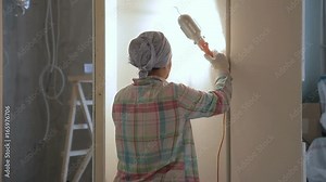 Woman master polishes wall with grinding instrument standing indoors. She deftly using abrasive tool