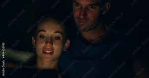 Bringing tech into the bedroom. A young happy smiling couple using a laptop in bed at night at home. Smiling man and woman relaxing in the bedroom with a computer together online