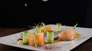 Slow motion restaurant cooking video. Close-up shot of chef pouring extra virgin olive oil on fish snack served with vegetables. Sliced herring put on white plate. Full hd