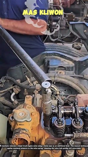 A mechanic removes a diesel truck engine valve using a metal pipe.