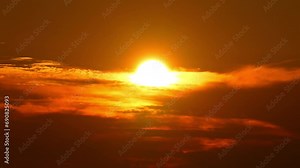 Timelapse of the sun setting in an orange yellow red sky, depicting an epic scene with the sun as bright and hot disk. The vibrant color sun hiding in the cinematic clouds, beauty of the summer sky