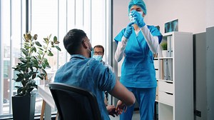 Rear Of Hindu Young Female Nurse Specialist In Uniform Making Coronavirus Vaccine Injection To Male Patient Sitting In Cabinet In Hospital While Doctor Working Behind, Covid Vaccination Concept | Free Stock Video Footage