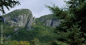 Two granite mountains covered in vegetation as branches lie in the foreground creating a sense of depth.