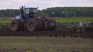 Download Blue New Holland tractor with double wheels pulling disc harrow with roller basket at spring day with slow motion