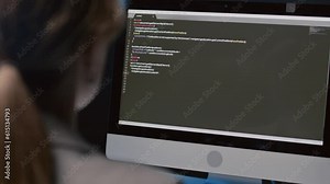 Over-the-shoulder close up of female programmer sitting at desk writing code in office at night