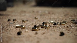 A close-up shot of bullet shells falling on the sandy ground. The bullet shells bounce off the floor as they land. Stock Video