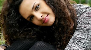 Portrait of a pretty young woman with beautiful curly hair putting head on her knees, slow motion