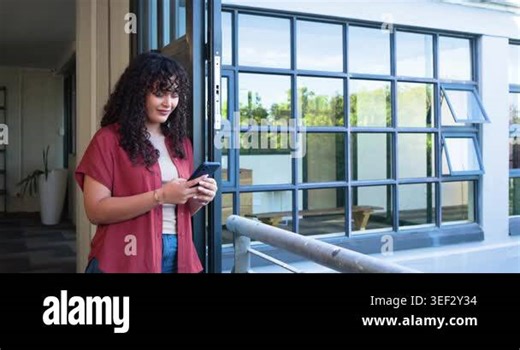 Woman holding smartphone, reading message, smiling and laughing, leaning at office door, copy space. Balcony, windows, daylight, greenery, joy, casual, workspace Stock Video Footage - Alamy