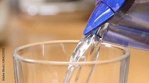 Pouring clean water from filter container into glass. Water filtration process at home