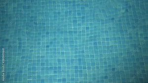 Looking down into a swimming pool at night at the refracted pool tiles on the base as they are distorted by the waters gentle turbulent flow. Lit within by the inner pool light.