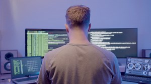 Premium stock video - A man at work , using multiple monitors showing graphs, debug windows, source code