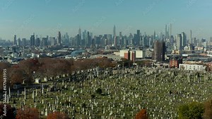 Forwards fly above historic Calvary Cemetery with tall modern high rise buildings in background. Queens, New York City, USA