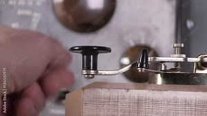 Extreme close-up of equipment settings and telegraph keying to send morse code radio transmission with vintage electronic hardware engineering military lab test equipment device in the background