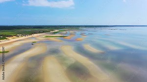 Scenic Cape Cod public beach captured by drone at ebb tide, where tidal pools shine across the sand and a parking lot filled with cars connects visitors directly to the natural shoreline.