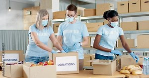Multi-ethnic busy charity organization workers man and women work in warehouse packing box parcel with donations sorting food. Volunteer activity, donating and volunteering, social help, covid-19