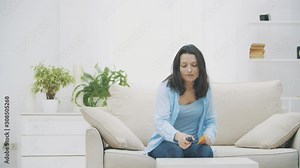 Slow motion. Attractive woman is switching on the TV with anticipation, holding an oranger paper sticker in her hand. Copy space. 4K.