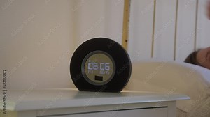 Female turning off the ringing digitall alarm clock on a bedside table at 6 in the morning