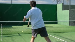 Two friends play paddle tennis on a sunny outdoor court, with one making a powerful shot. Dynamic sports action in a casual setting