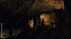Tourists wearing masks exploring Coves d'Artà rocky formations of stalactites and stalagmites. Underground natural cave scenery with cavities of carbonate limestone in Mallorca, Balearic Spain