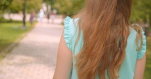 Closeup back view portrait of young long haired beautiful female walking with her hair flattering in wind in park outdoors
