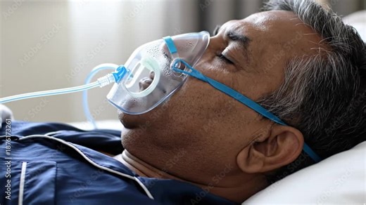 An elderly man lies on a hospital bed wearing a cpap oxygen mask on his face for breathing treatment