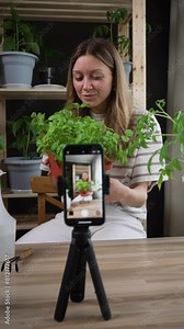 Young woman discussing gardening techniques on camera, surrounded by her collection of healthy indoor plants, creating educational content. Blogger records video for publication on social networks.