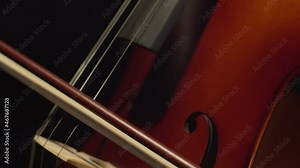 Bow plays on strings of cello reproducing classical music, closeup. Musician plays bow on strings of musical instrument while performing at concert. Concept art and music