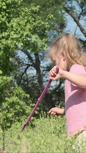 VERTICAL VIDEO: Little girl tries to catch butterfly on butterfly net in city park. Cute little girl catching butterfly on aerial insect net in meadow on sun day. Slow motion