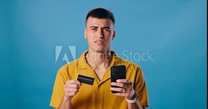 Confused, mobile phone and man with credit card in studio for online shopping, debt or transaction on blue background. Payment, scam and face of person for problem, subscription or internet banking