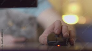 A man's hand on a computer mouse presses the buttons and turns the wheel, works in the evening at home, on a blurred background a British cat sits