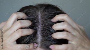 Young woman with dirty greasy hair on a grey background. A girl itching the skin from long non-washes of the head. Close up. Girl applying cosmetic oil rubbing it into a scalp with her hands