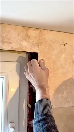 A person is carefully applying tile adhesive to a wall using a trowel