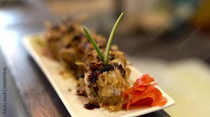 On the foreground we see a plate with sushi. On the background chef is doing some preparations.