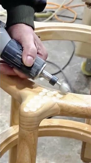 The craftsman meticulously utilizes a rotary tool to effectively carve a wooden chair component