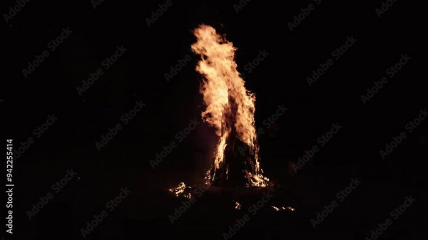 A tall burning pyre burns under the open sky at night. Fire burning on a summer evening for atmosphere in a group of friends. Wood burning lighting up the dark night sky and creating a beautiful scene