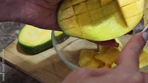 After the ripe orange mango has been cut open, use a spoon to scrape out the pulp. And put the juicy pulp into a clear plate. Cutting a ripe mango with the pit. Close-up in the kitchen