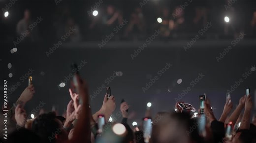 Fans lift smartphones and hands toward stage capturing powerful live concert moment with flashing strobe lights and dynamic atmosphere