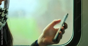 Candid 4K clip of woman checking her cellphone while on a moving train with background landscape in motion